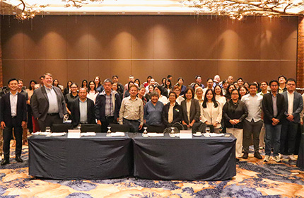 Group photo of workshop participants standing behind draped tables in a hotel function room.